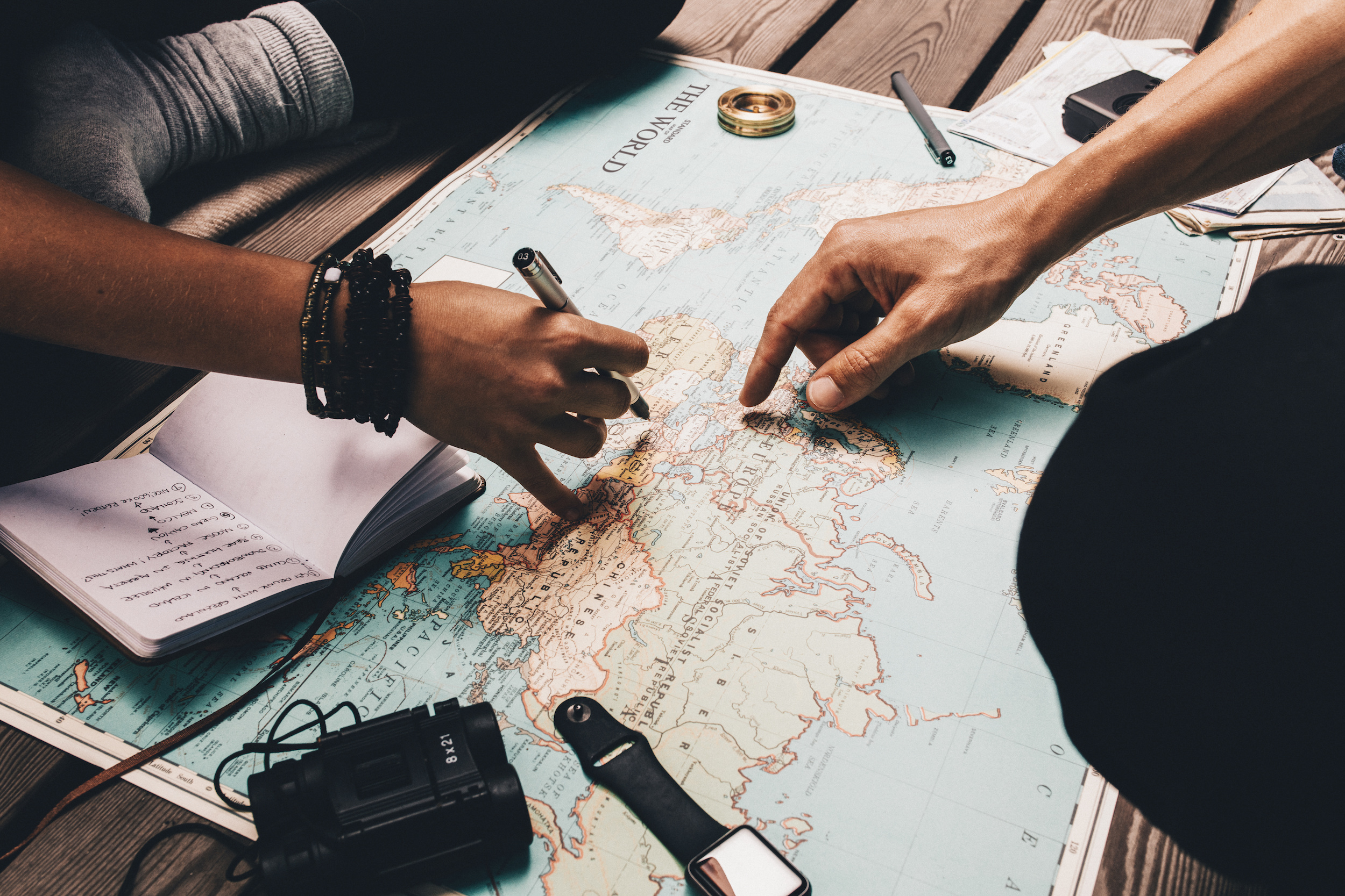 Close up view of man and woman pointing at places on world map. Woman noting vacation plan in a diary.